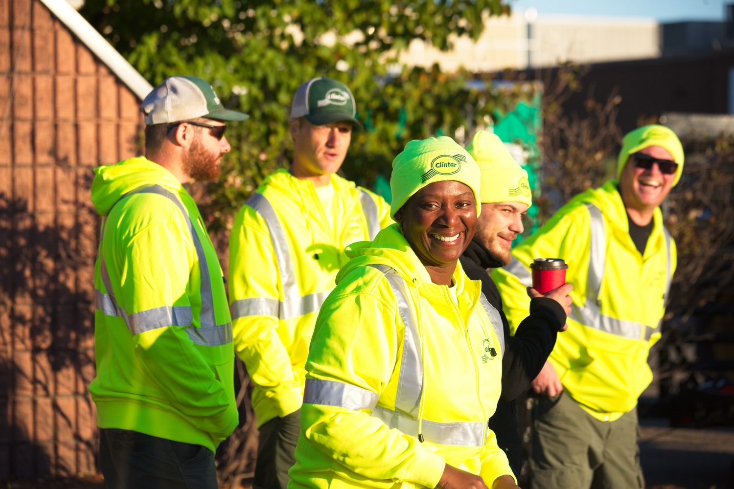 Five Clintar employees in bright yellow safety jackets stand outside smiling and laughing.